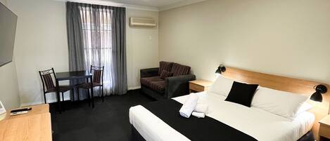 A hotel room with a large bed, a desk, a chair, and a small table.