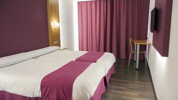 Une chambre d’hôtel avec deux lits, un bureau, une chaise, une télévision et un rideau.