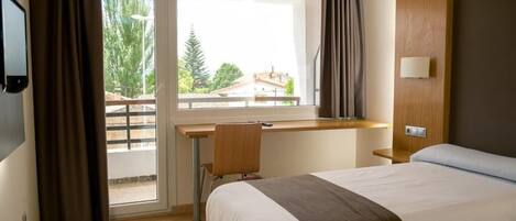 Una habitación de hotel con cama, escritorio y ventana con cortinas.