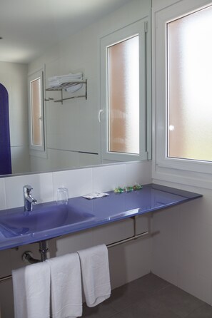 A bathroom with a blue sink, white tiles, a mirror, and frosted glass windows.