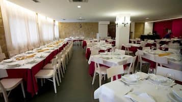 A banquet hall with rows of tables set for dining, white chairs, and red tablecloths.