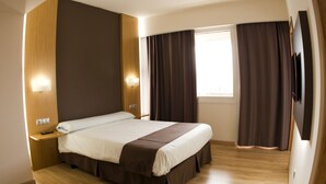 Ein modernes Hotelzimmer mit einem großen Bett, Holzboden und einem Flachbildfernseher.
