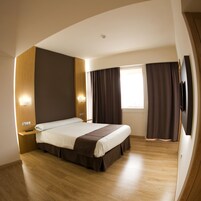 Quarto de hotel moderno com uma cama grande, piso de madeira e televisão de tela plana.