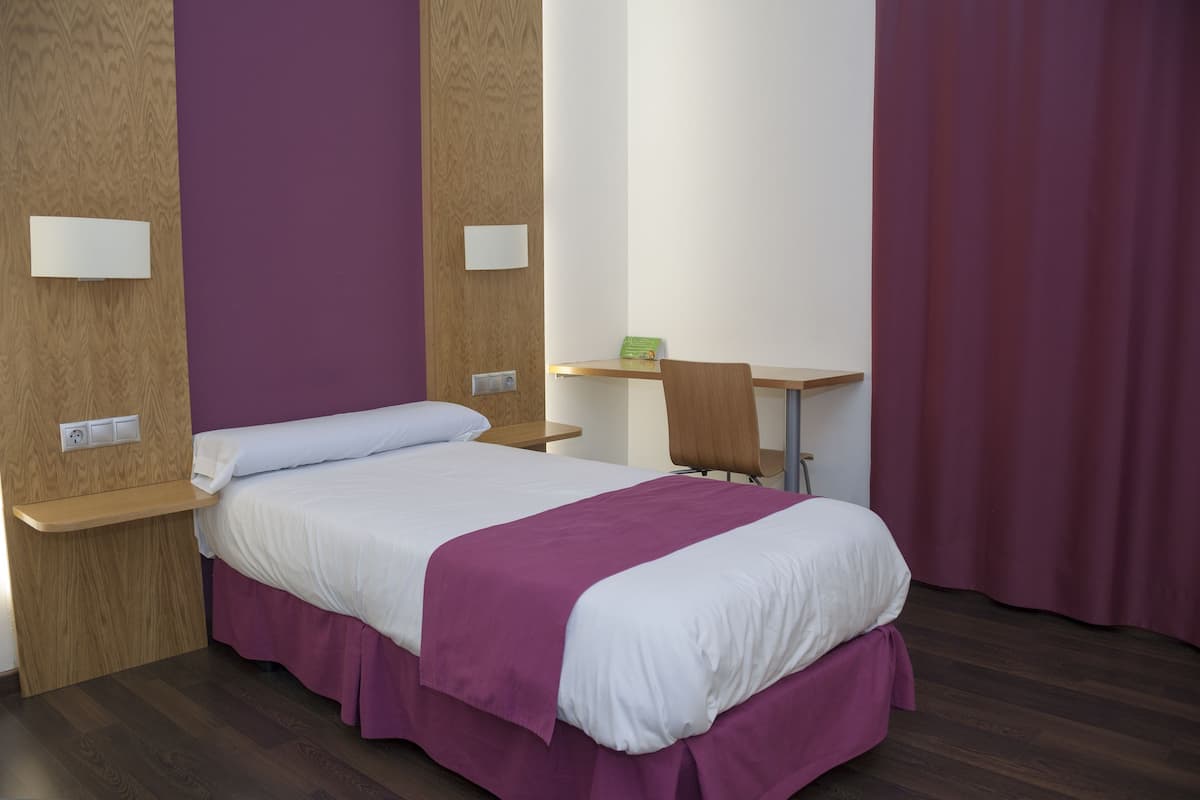 A hotel room with a bed, a desk, and a chair.