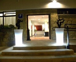 Entrada de hotel com paredes de pedra, uma escadaria e uma área de recepção visível pela porta.
