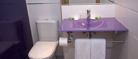 A bathroom with a white toilet, a purple sink, and a towel hanging on a rack.