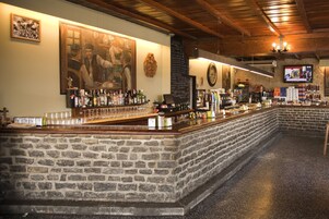Um bar com balcão de pedra, teto de madeira e uma tela de televisão.