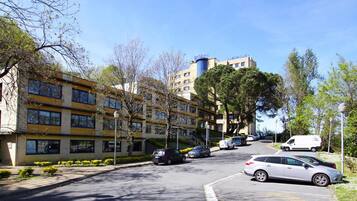 A multi-story hotel with a modern design, featuring a parking area with several cars and a white van.