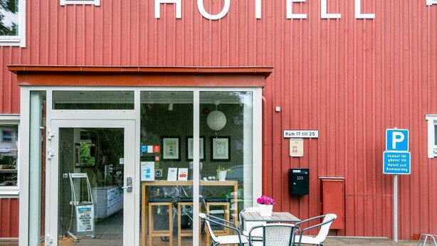 A red building with a glass entrance, a sign reading "HOTEL", and a small outdoor seating area with a table and chairs. - Ett Smart Sollentuna (Sollentuna)