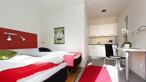 A modern hotel room with a bed, a desk, and a kitchenette.
