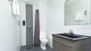 A modern bathroom with white tiles, a grey shower curtain, a white toilet, and a dark wooden vanity with a black sink. - Ett Smart Sollentuna (Sollentuna)