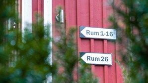 A red building with two directional signs indicating 'Rum 1-16' and 'Rum 26'. - Ett Smart Sollentuna (Sollentuna)