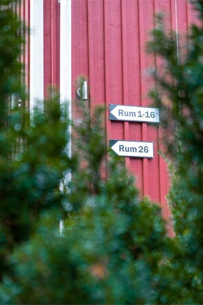 A red building with two directional signs indicating 'Rum 1-16' and 'Rum 26'. - Ett Smart Sollentuna (Sollentuna)