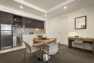 Une cuisine moderne équipée d’appareils électroménagers en acier inoxydable, un coin repas avec une table ronde et des chaises, et un bureau avec un fauteuil.
