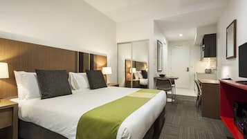 A hotel room with a large bed, a desk, a TV, and a mirror.