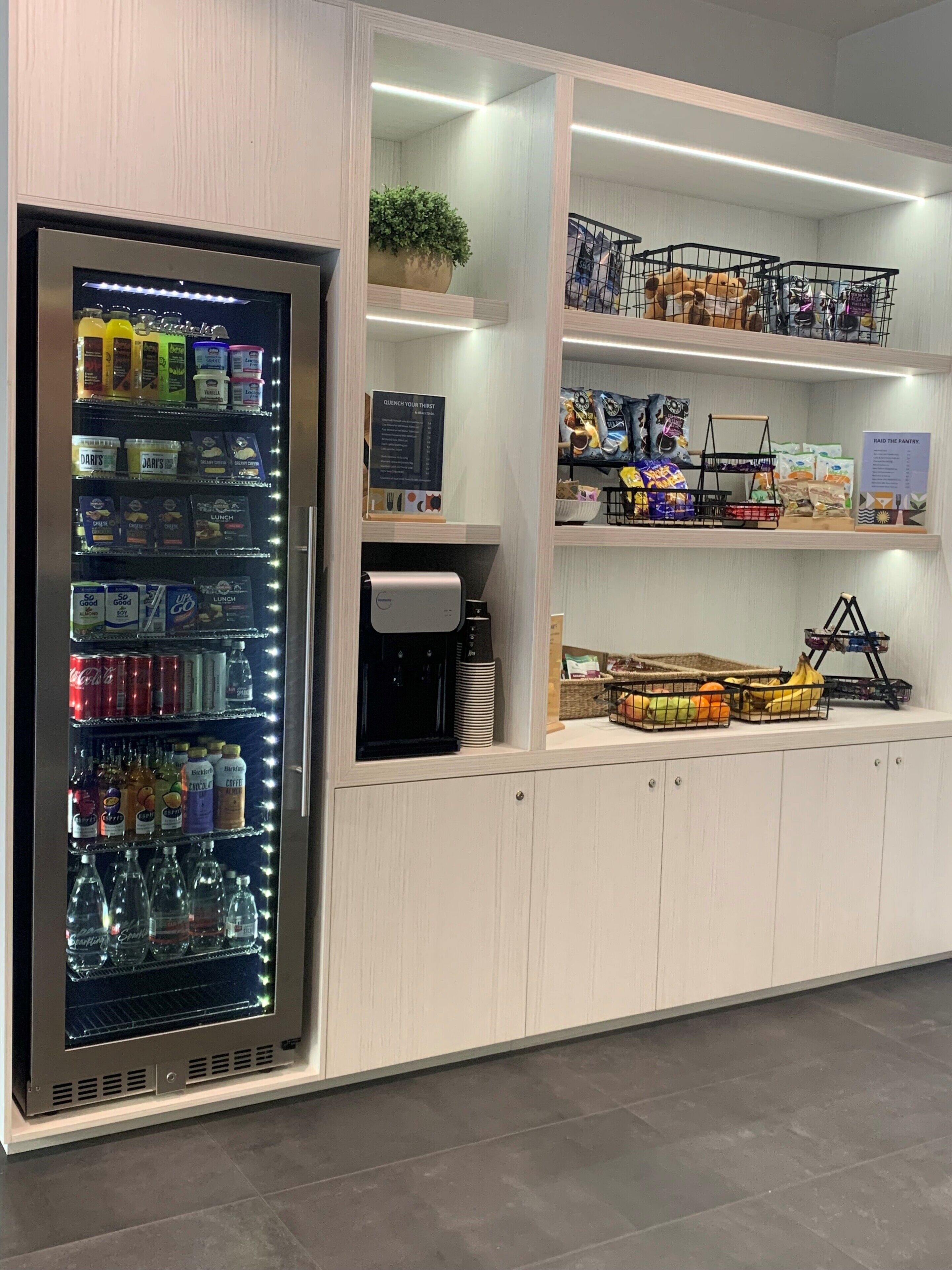 Ein Getränke- und Snackautomaten, eine Kaffeemaschine sowie Regale mit verpackten Lebensmitteln und Obst.