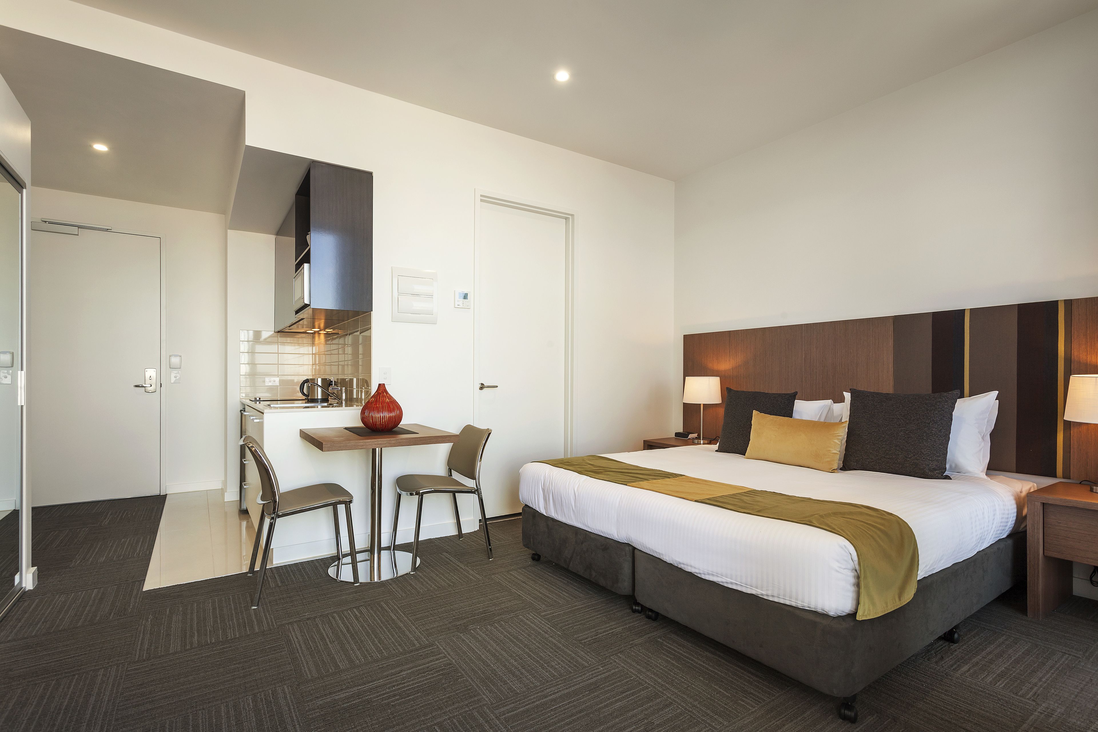 A hotel room with a bed, a desk, a chair, and a kitchenette.