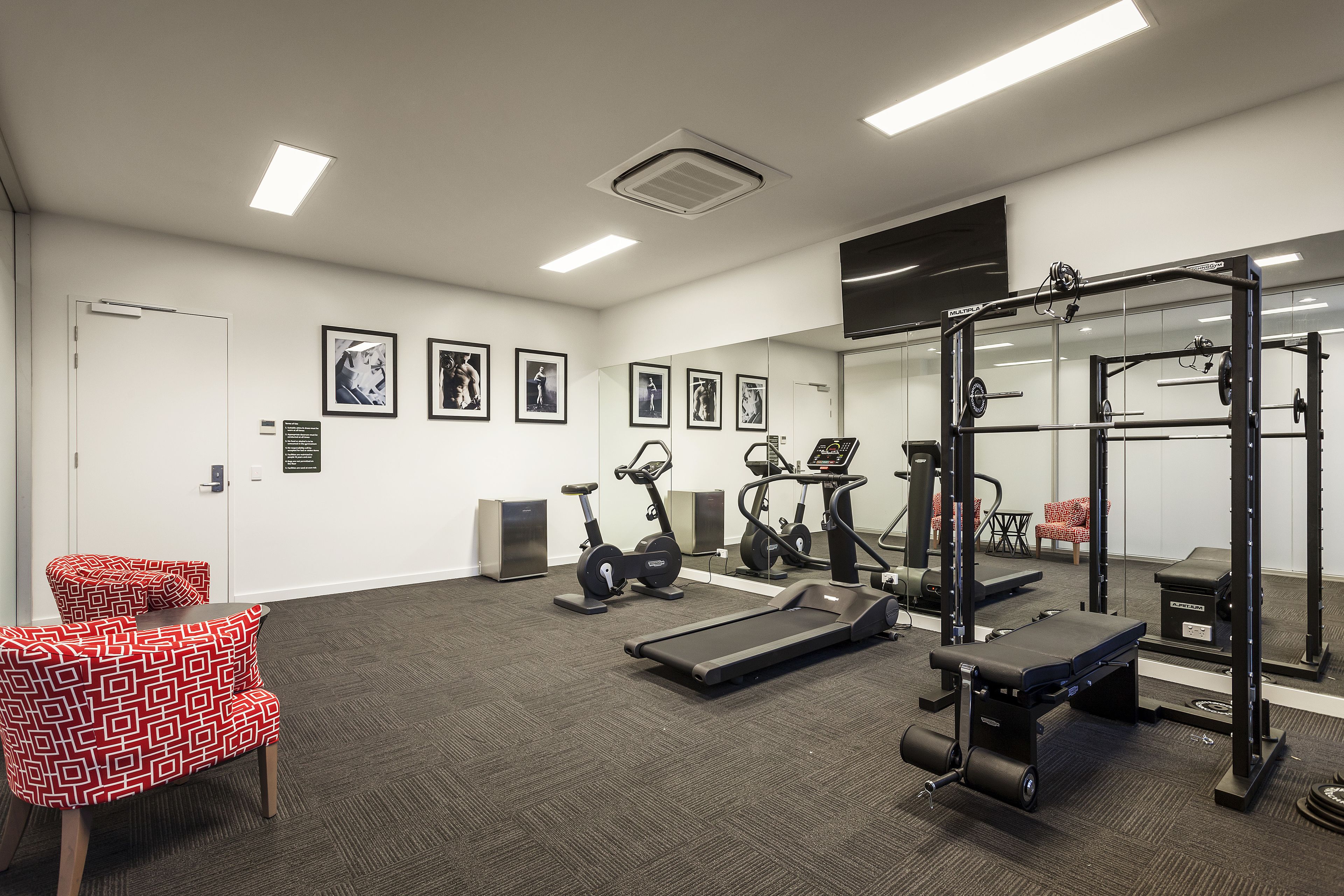 Une salle de sport équipée de matériel d’exercice, d’un tapis de course et d’un mur recouvert de miroirs.