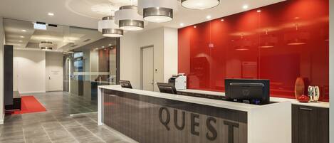 A modern reception desk with the word "QUEST" prominently displayed, a glass partition, and a red accent wall.