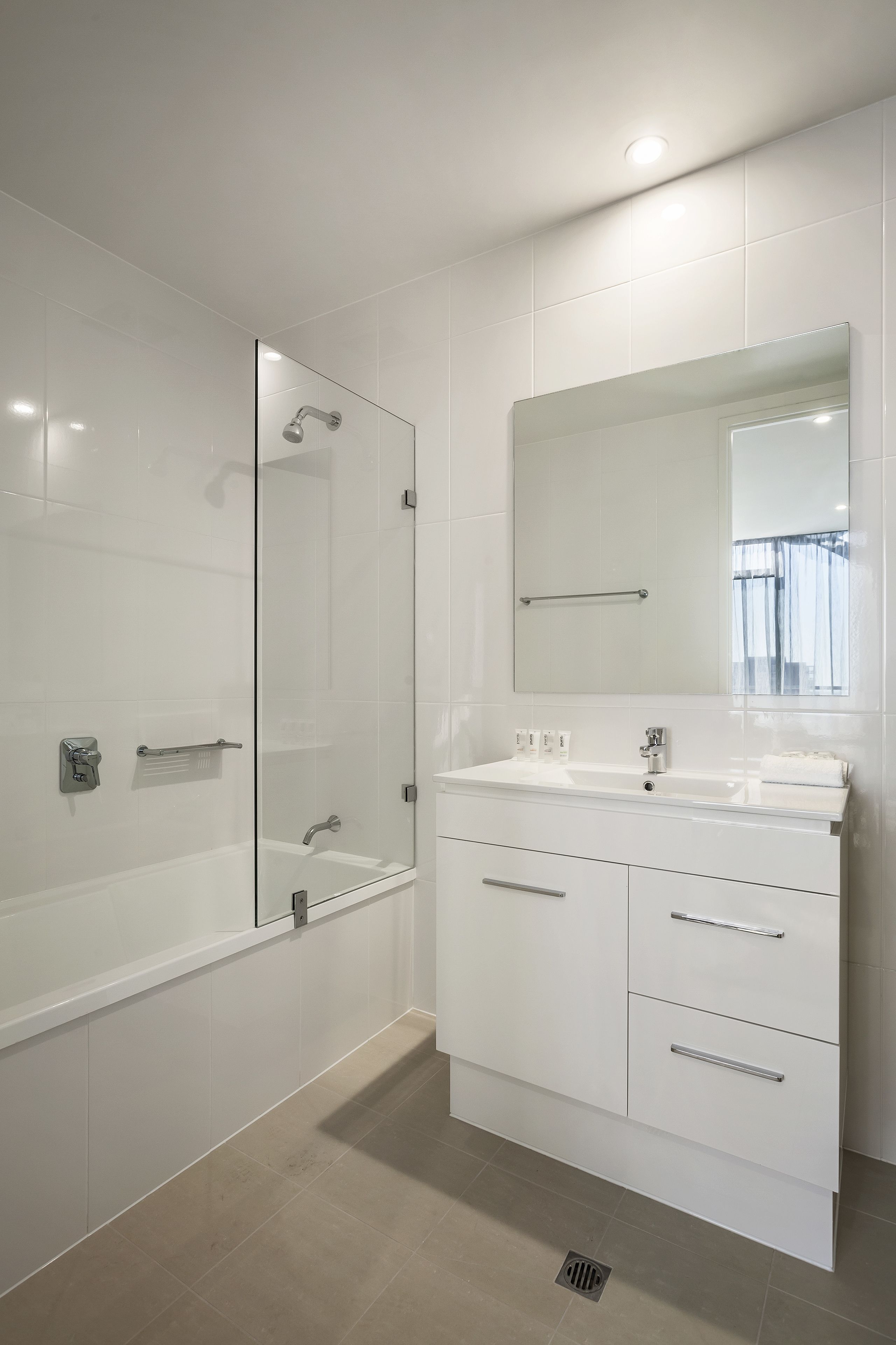 A modern bathroom with a glass shower enclosure, a large mirror, and a white vanity with drawers.