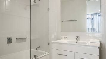 A modern bathroom with a glass shower enclosure, a large mirror, and a white vanity with drawers.