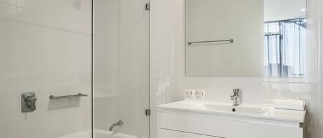 A modern bathroom with a glass shower enclosure, a large mirror, and a white vanity with drawers.