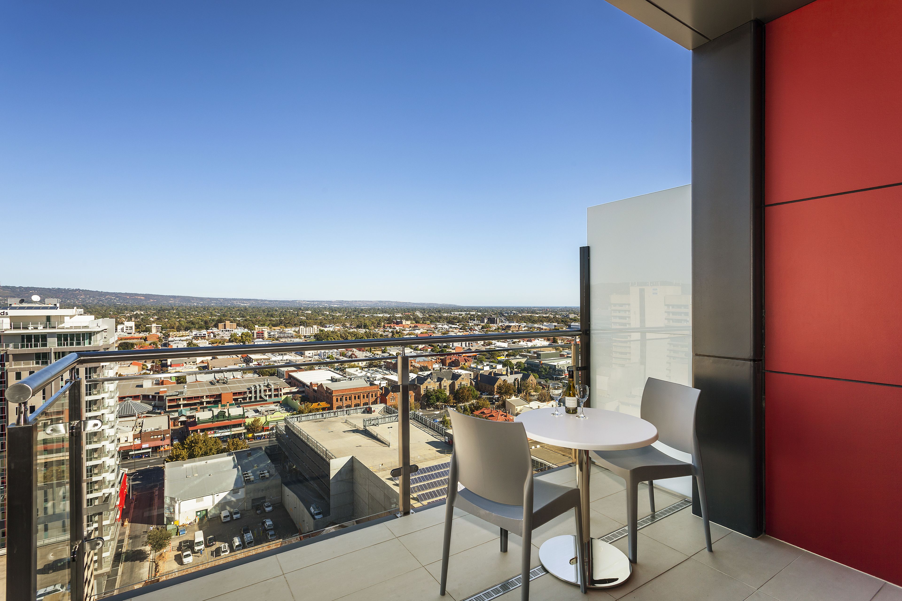 A balcony with a table and chairs, overlooking a cityscape with buildings and a clear sky.