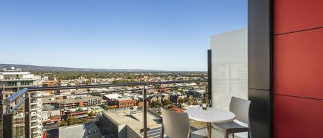 A balcony with a table and chairs, overlooking a cityscape with buildings and a clear sky.