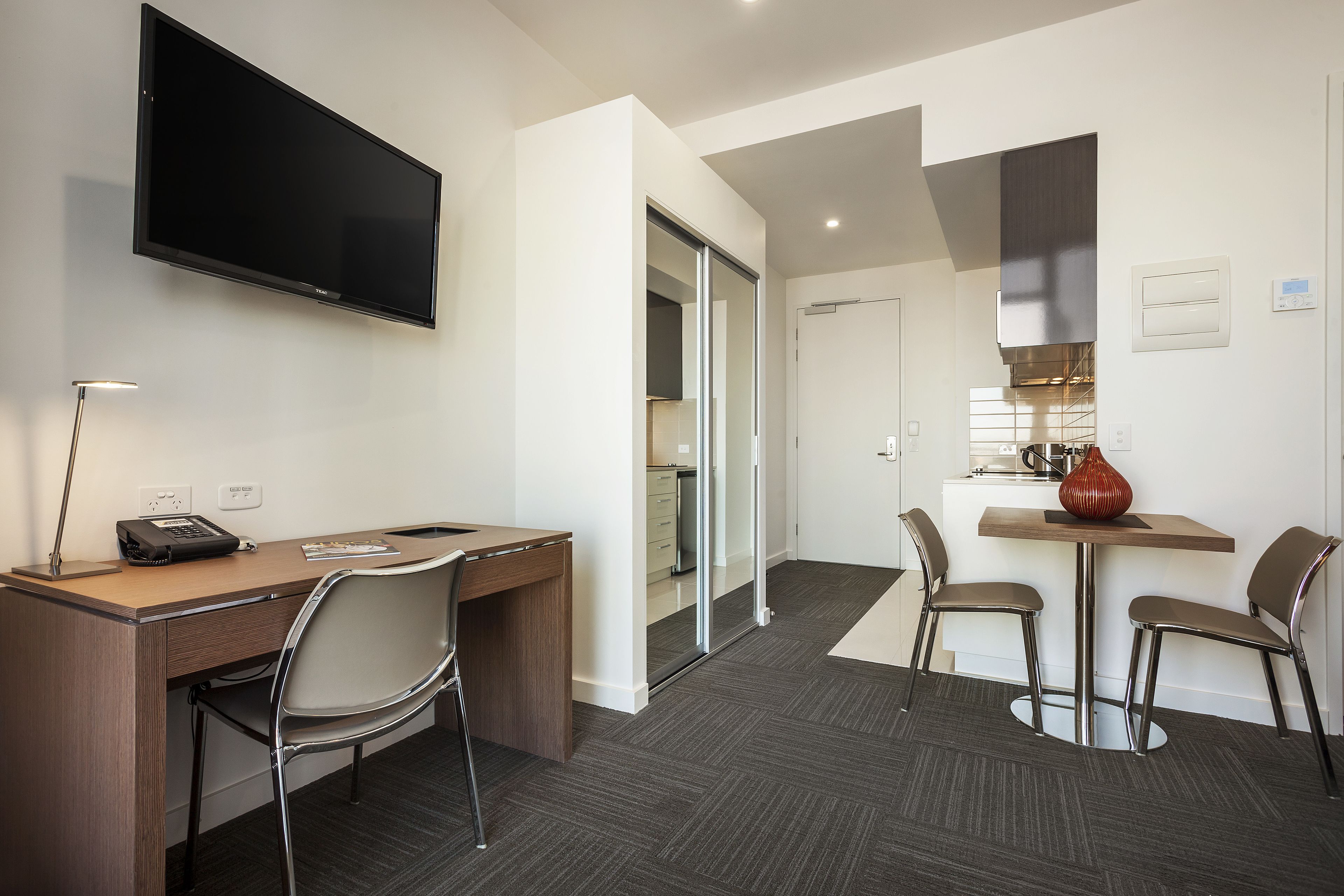 A hotel room with a desk, chair, TV, and a dining area with chairs and a table.