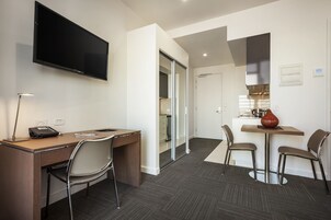 Une chambre d’hôtel équipée d’un bureau, d’une chaise, d’une télévision et d’un coin repas avec des chaises et une table.