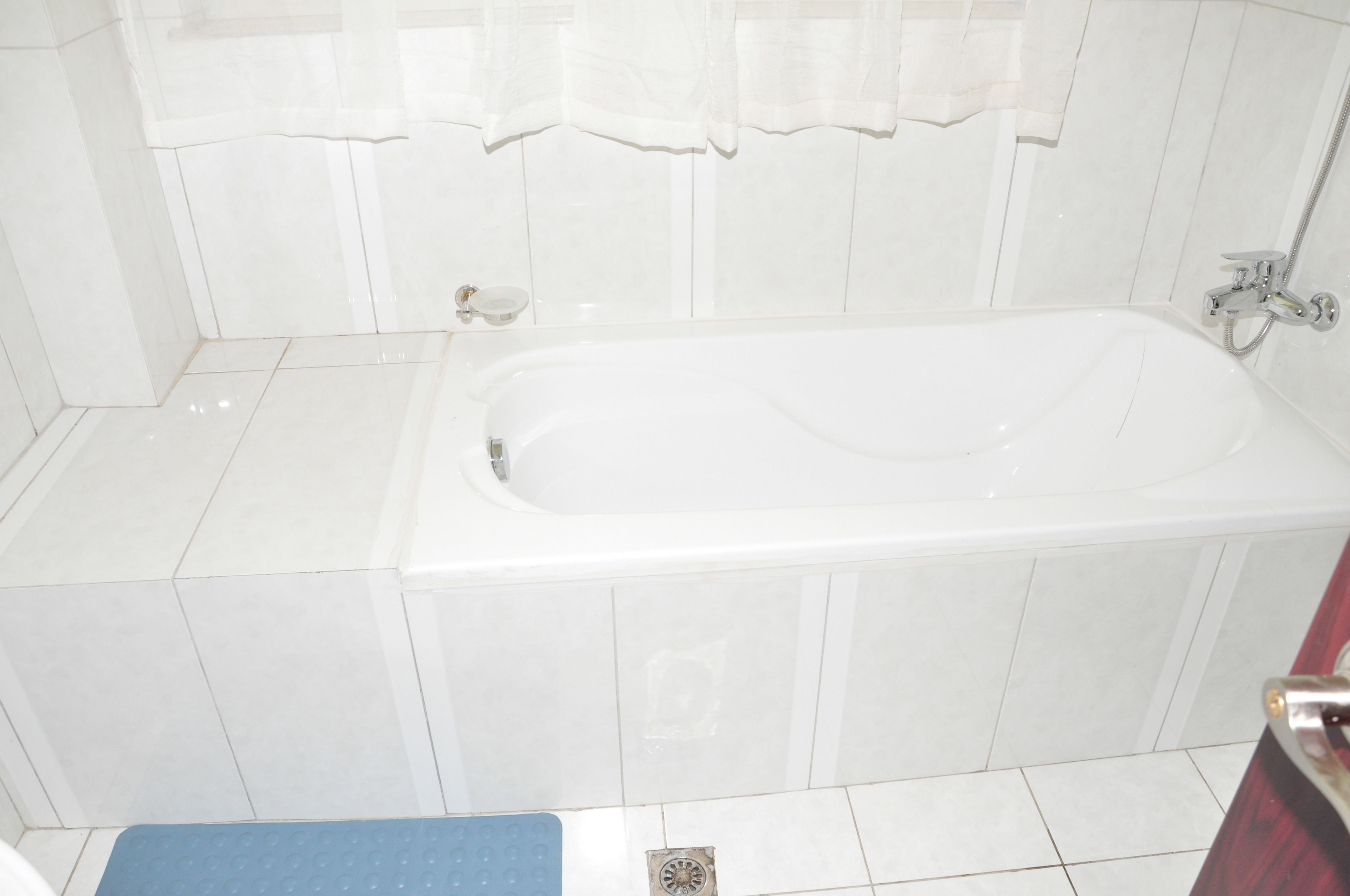 Un bagno con una vasca da bagno bianca, piastrelle bianche sulle pareti e un tappetino blu sul pavimento.