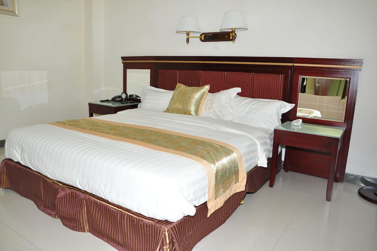 A hotel room with a large bed, a nightstand, a bedside table, a mirror, and a wall-mounted lamp.