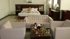 Habitación de hotel con una cama grande, dos mesitas de noche, un sofá, una mesa de centro y una lámpara.