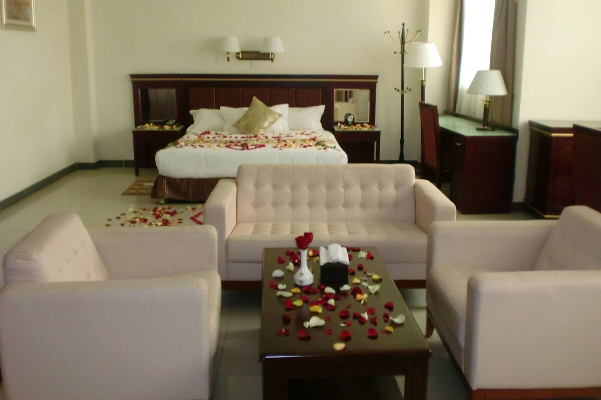 A hotel room with a large bed, two bedside tables, a sofa, a coffee table, and a lamp.