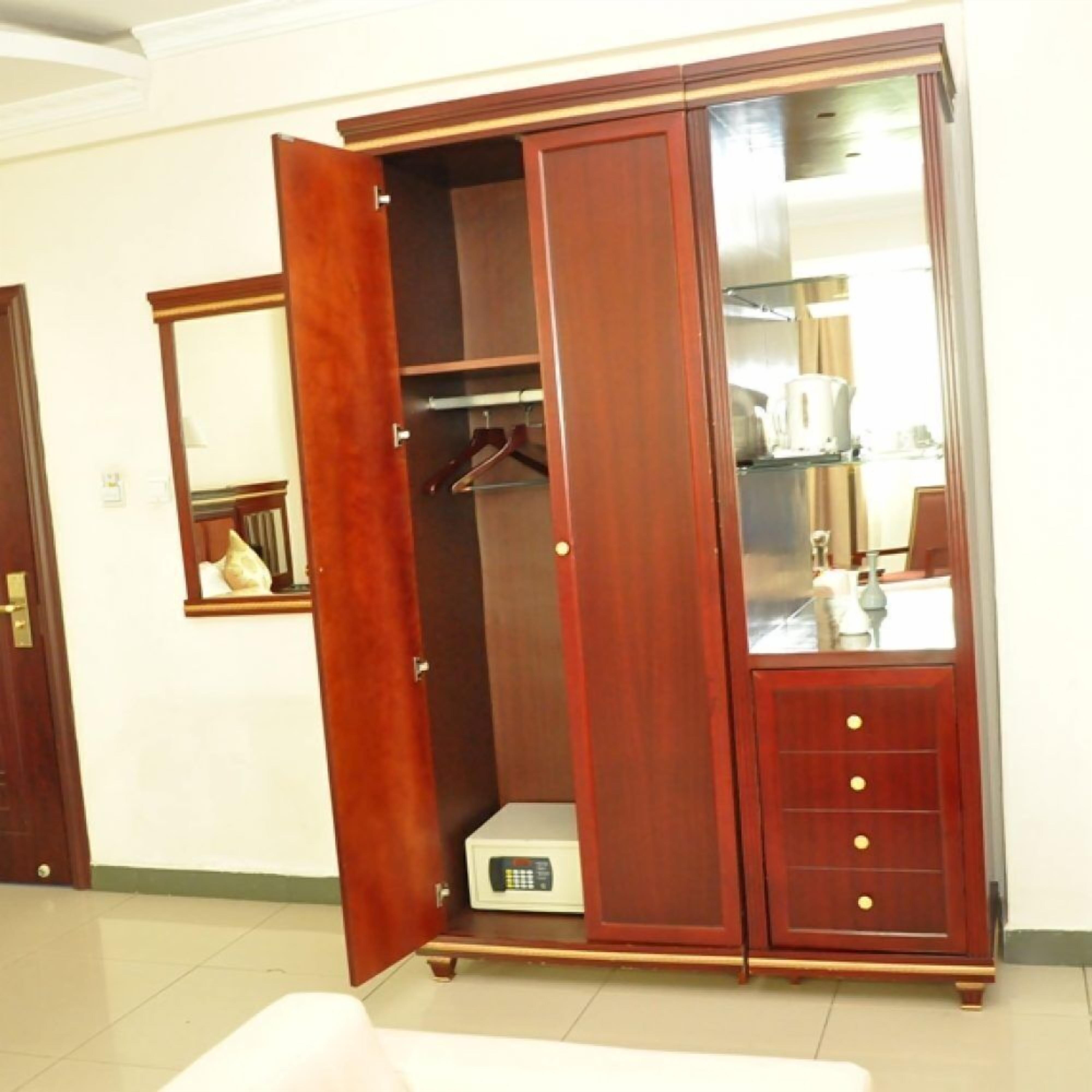 A wooden wardrobe with a mirror and a small control panel, likely for climate control, in a hotel room.