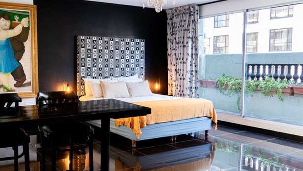 A hotel room with a large bed, a dining table, a chandelier, and a view of the outside.