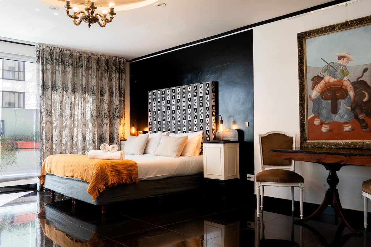 Un dormitorio moderno con una cama grande, una mesita de noche, una silla, una mesa y un cuadro en la pared.