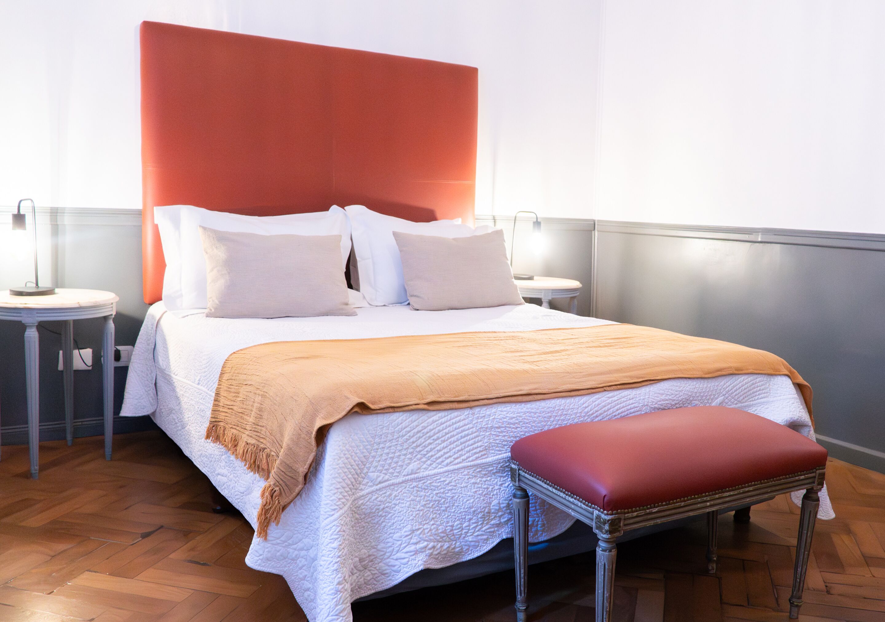 A neatly made bed with a red headboard, white bedding, and a red bench at the foot of the bed.