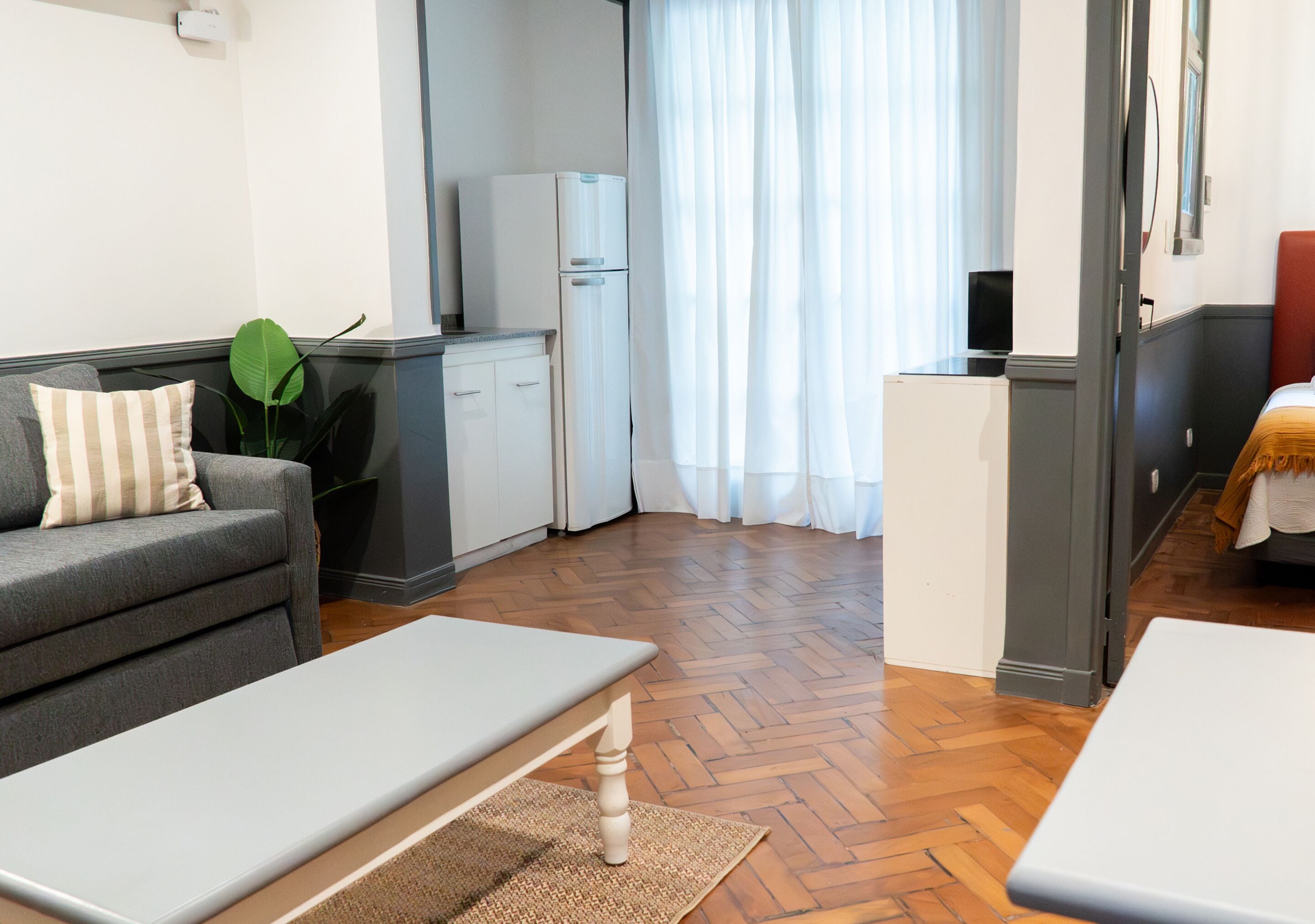 A compact living space with a sofa, a small dining table, a kitchenette, and a view through a window with curtains.