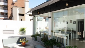 An outdoor patio with seating, planters, and a glass wall reflecting the surroundings.