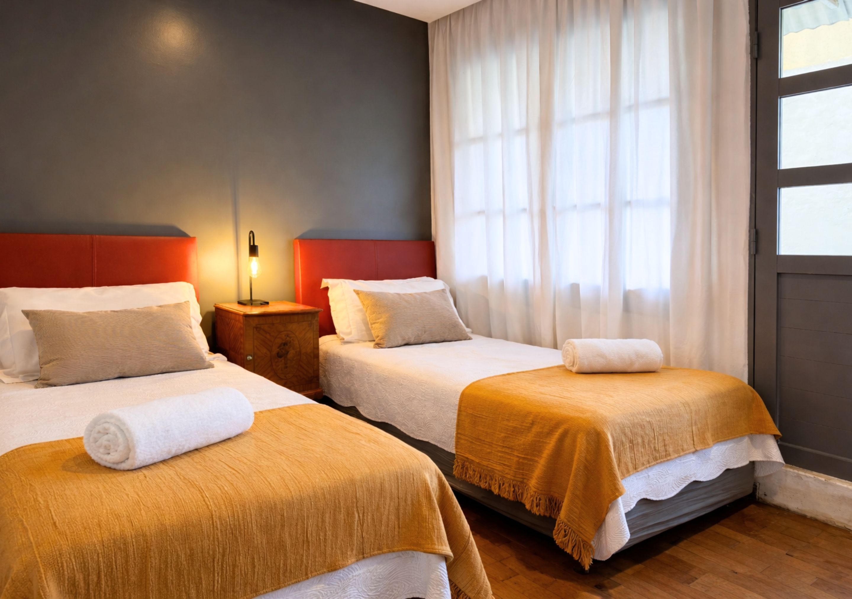 A hotel room with two beds, a nightstand, a lamp, and a window with curtains.