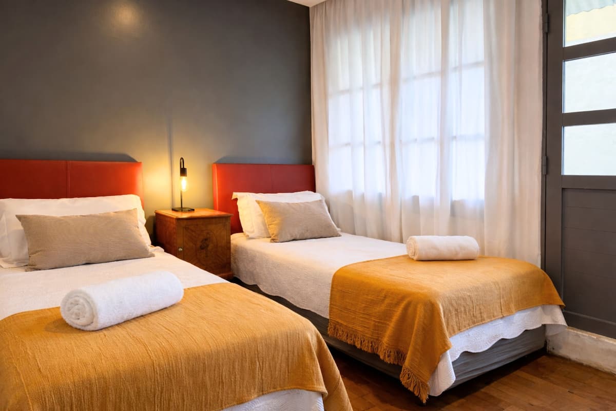 Una habitación de hotel con dos camas, una mesita de noche, una lámpara y una ventana con cortinas.