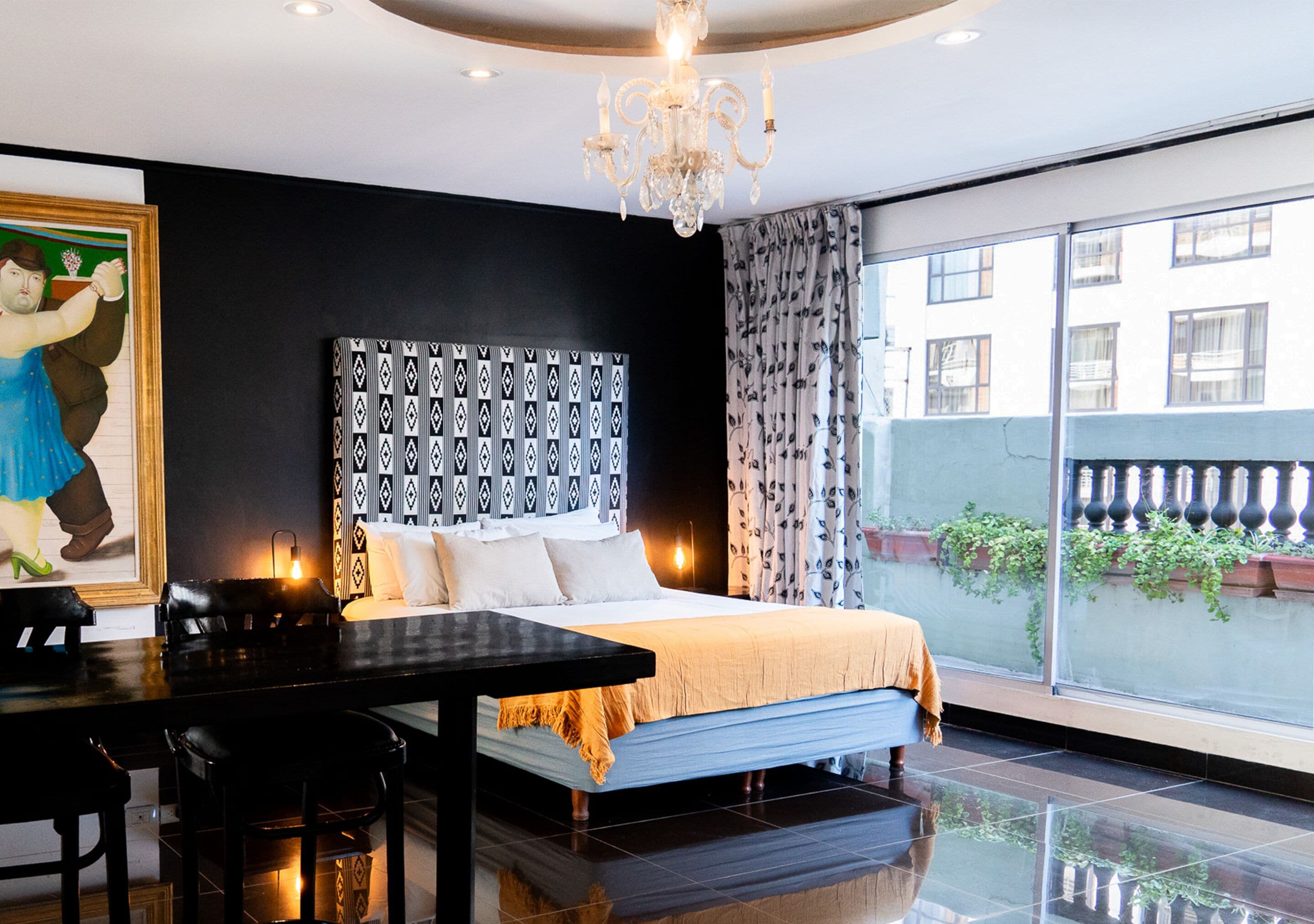 A hotel room with a large bed, a dining table, a chandelier, and a view of the outside.