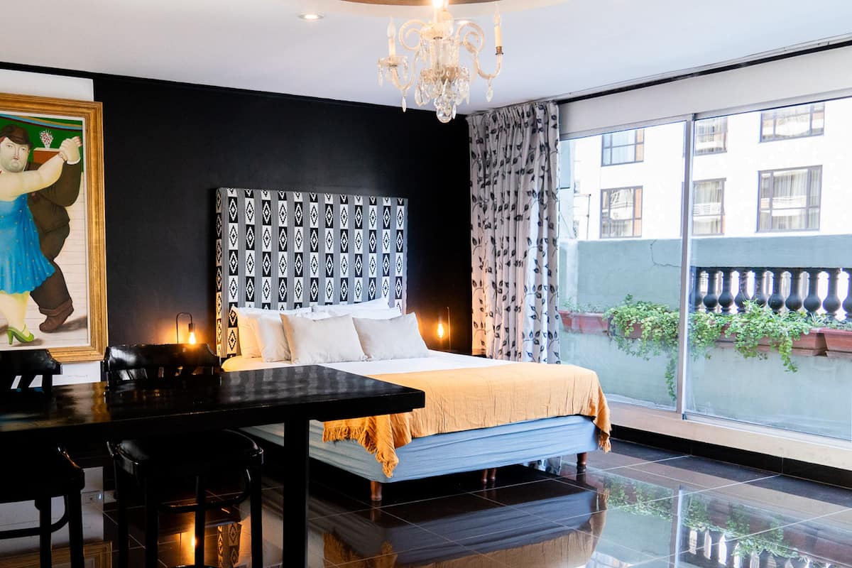 Habitación de hotel con una cama grande, una mesa de comedor, una araña y vistas al exterior.