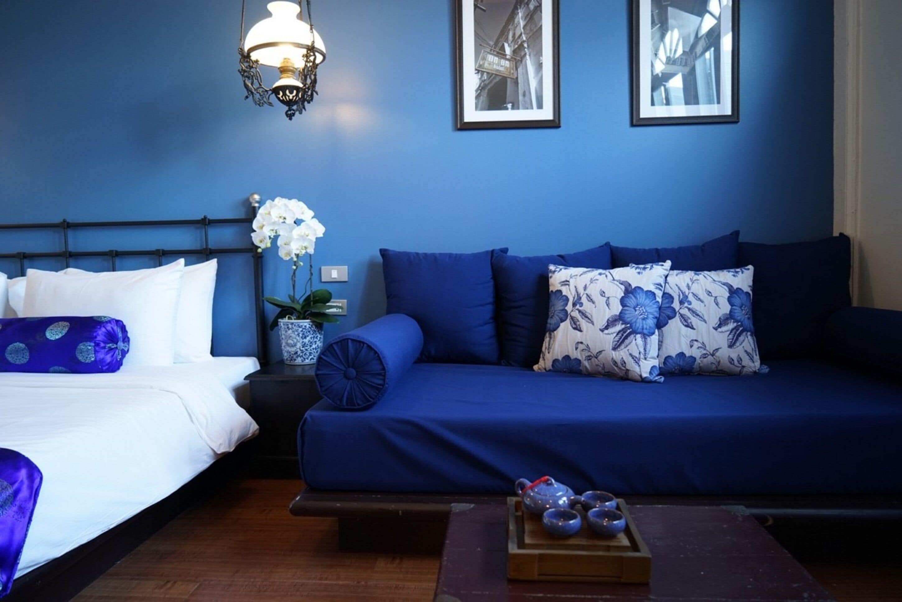 Une pièce comprenant un lit, un canapé bleu, une table de chevet avec une lampe et un tableau encadré accroché au mur.