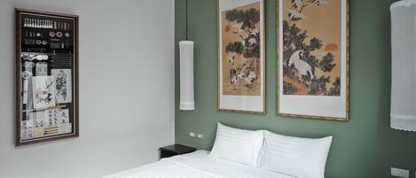 Un lit bien fait dans une pièce aux murs verts, avec deux œuvres d’art encadrées représentant des oiseaux et un panneau décoratif fixé au mur.