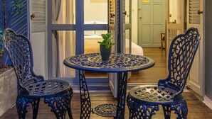 A patio with two ornate metal chairs and a small table, a potted plant, and a view into a room with a bed and a door. - The Memory at On On Hotel (Phuket)