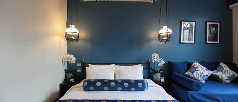 A bedroom with a bed, a sofa, two wall-mounted lamps, and framed pictures.