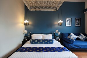 Un dormitorio con cama, sofá, dos lámparas de pared y cuadros enmarcados.