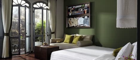 A bedroom with a large bed, a sofa, a small table, and a wall-mounted TV.